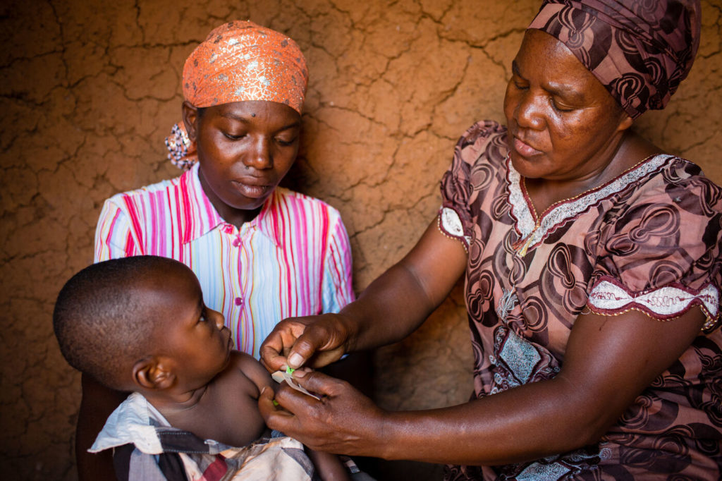 One-year-old Shukulu Nibogore sits on her mother’s lap while Athanasie Mukamana, a PIH community health worker in Rwanda since 2005, measures her arm for signs of malnutrition.