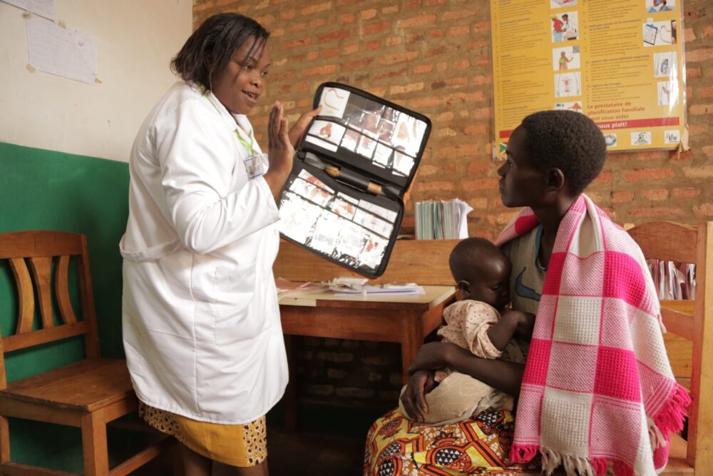A healthcare worker uses visual aids to explain family planning methods to a mother and her child in a clinic.